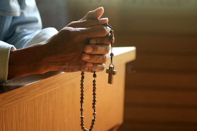 Senior man kneel, holding wooden rosary beads in hand with Jesus Christ holy cross crucifix in the church.