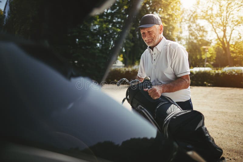 Senior man packing his golf clubs in a car trunk