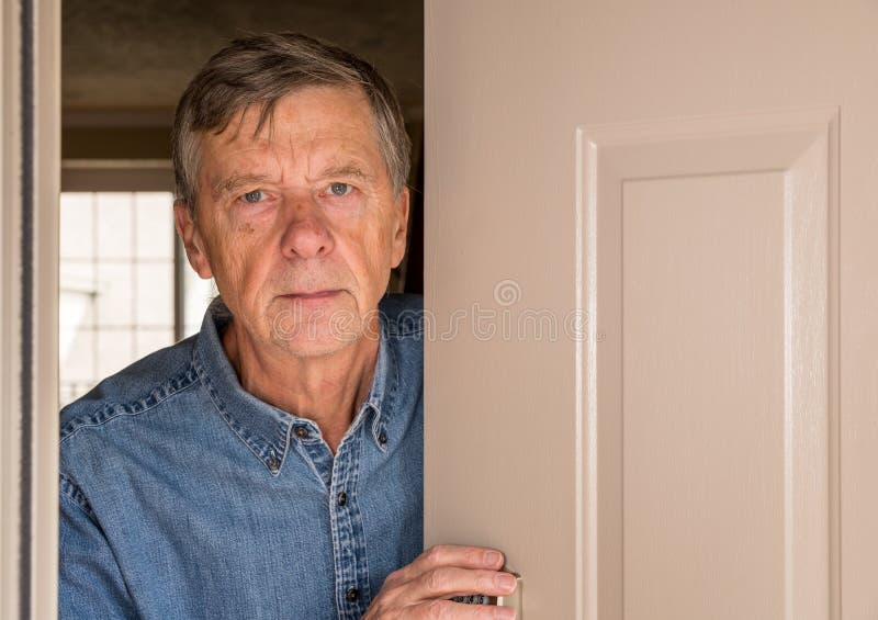Senior man peering through front door for visitors during quarantine