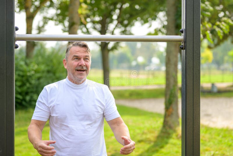 Senior man psyching himself up during an outdoor workout on exercise bars in a park standing ready to take hold