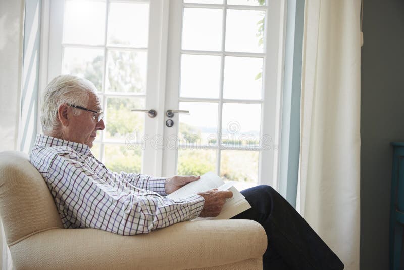 Senior man sitting in an armchair reading a book, close up