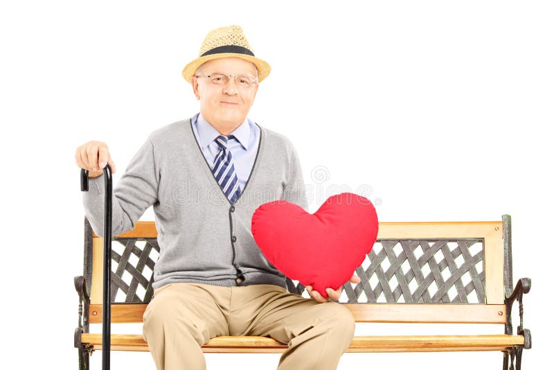 Senior man sitting on a wooden bench and holding a red heart