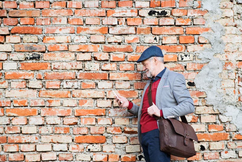 Senior man with smartphone against brick wall, texting.