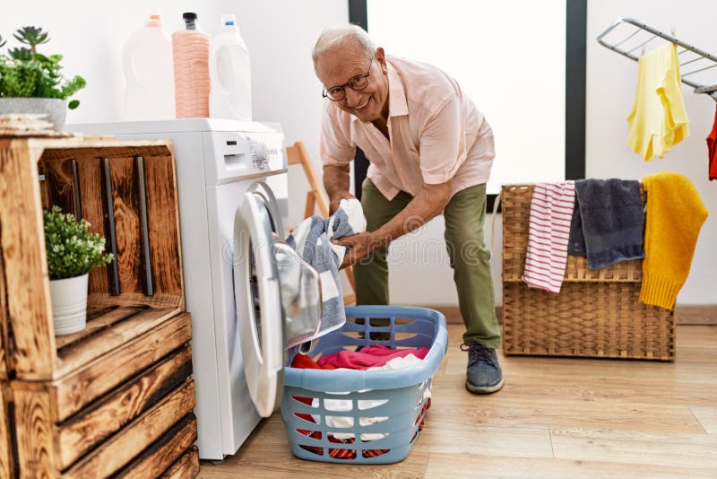 Senior Man Smiling Confident Washing Clothes at Laundry Room Stock