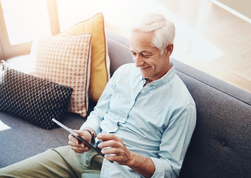Senior man, tablet and relax on sofa in home for typing email, communication and reading online news. Elderly person royalty free stock image