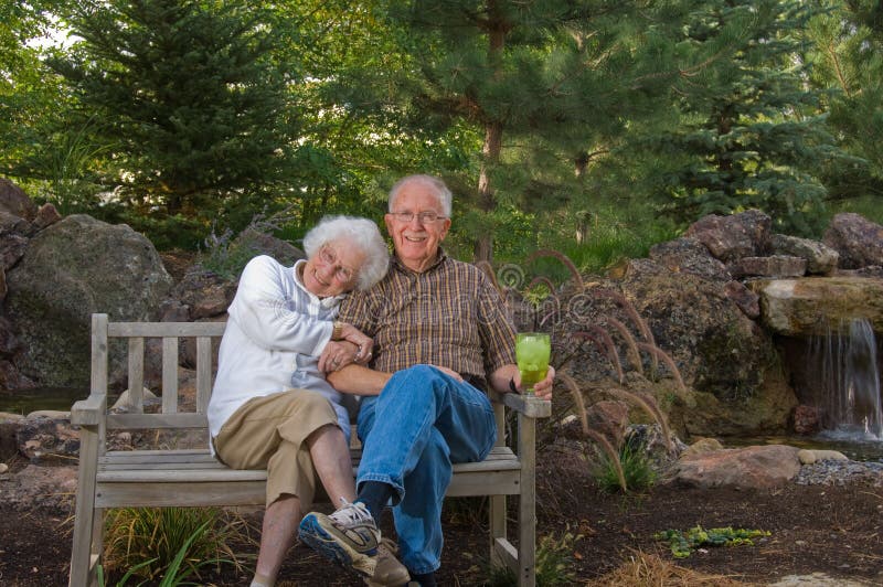 Senior man and woman sitting on a bench by a man-made pond and waterfall. Man made waterfall stock images, royalty-free photos and pictures