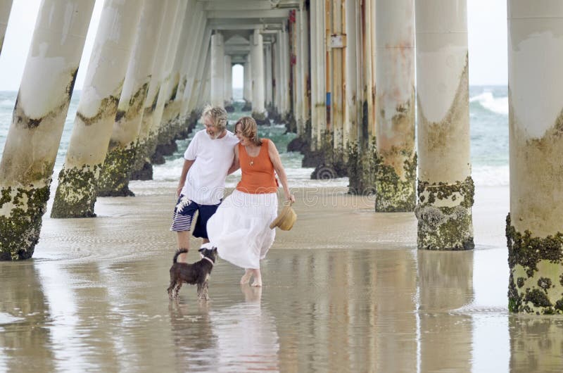 Una bella fresca e dolce ritratto di un senior maturi uomo e donna, a piedi molto vicino, a braccetto tenendosi per godere di una romantica e molto rilassante vacanza al mare sulla splendida Sputare sulla Gold Coast , in Australia, con la sua piccola simpatico cane da compagnia.