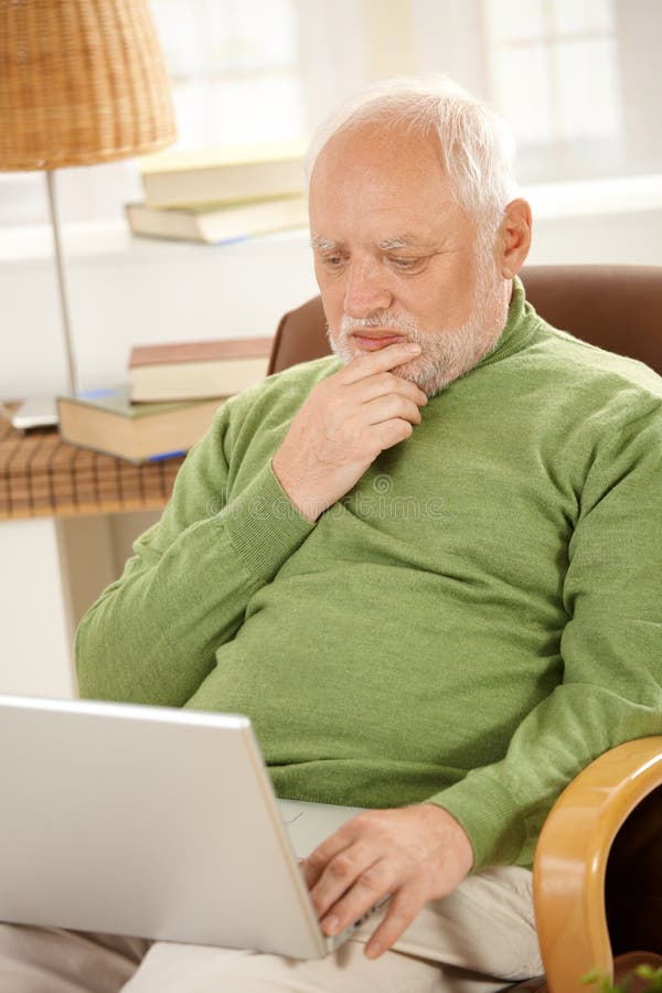 Senior man sitting at home, looking at screen of laptop computer, thinking.