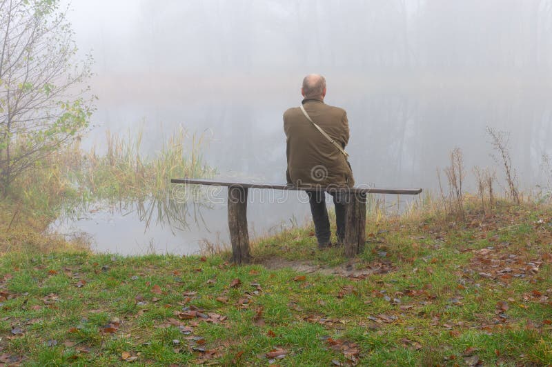 Senior Mann, einsam auf einer Bank am Flussufer sitzend