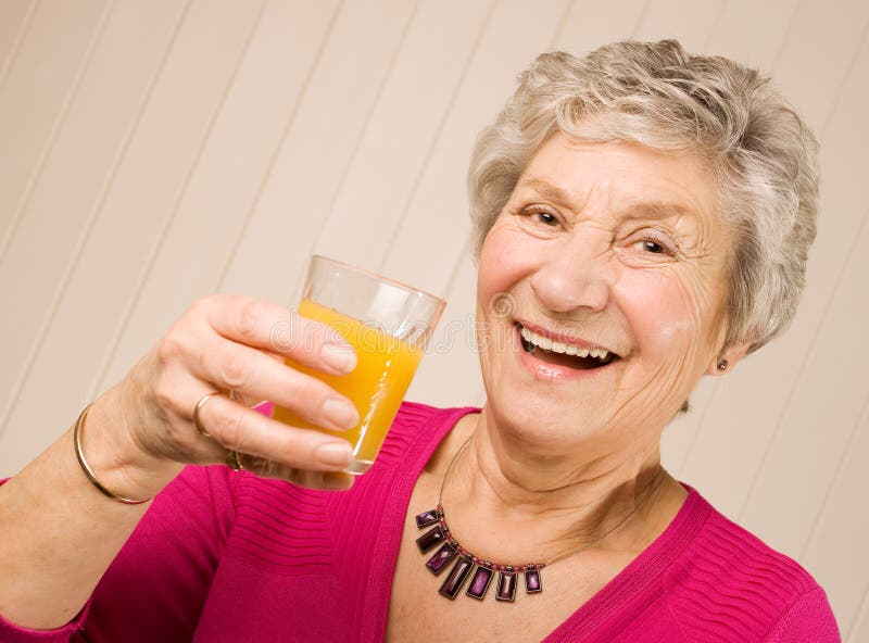 Happy senior mature lady holding glass of fresh orange juice 