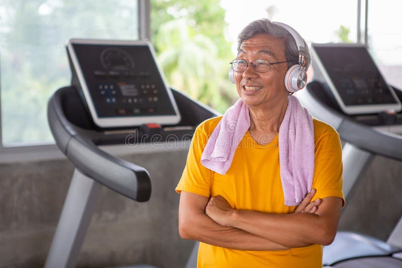 Senior older man taking a break from workout listening music with headphones relaxing in fitness gym. aged . Old male .Mature sport training.rehabilitation.elderly Healthy lifestyle, smile, aging, power, athlete, take, retirement, adult, happy, strength, earphones, rest, leisure, energy, activity, retired, repair, effort, cardio, retiree, asian, towel, people, exercise, pensioner, active, sportswear, equipment, indoors