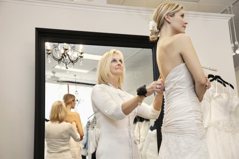 Senior owner assisting young bride getting dressed in wedding gown