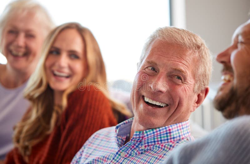 Senior Parents With Adult Offspring Sitting On Sofa At Home Talking And Laughing.