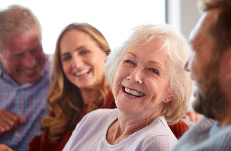 Senior Parents With Adult Offspring Sitting On Sofa At Home Talking And Laughing.