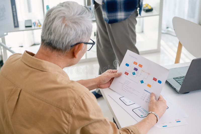 Senior programmer planning software development with flowchart and system process documentation at office stock photos