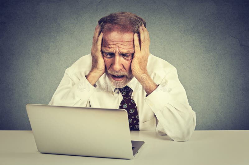 Senior stressed man working on laptop sitting at table