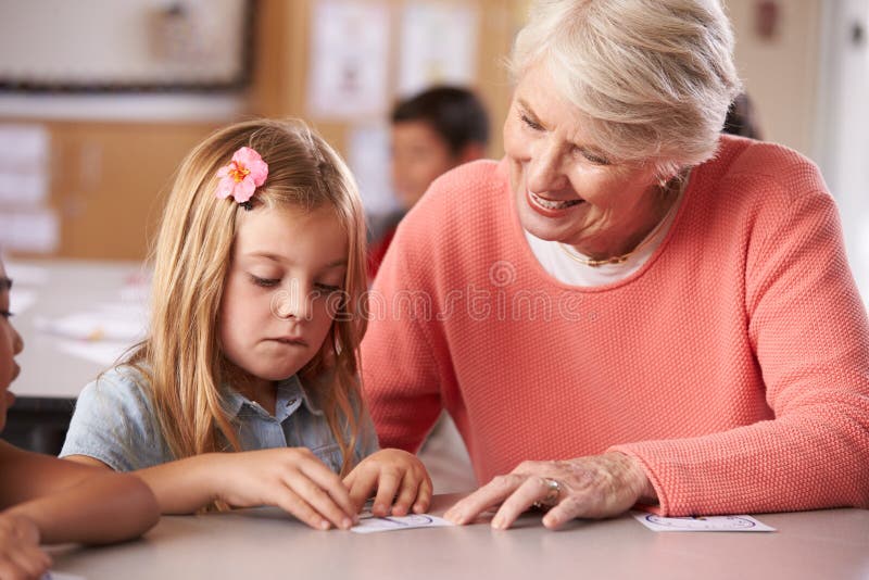 Senior teacher helping schoolgirl in elementary class