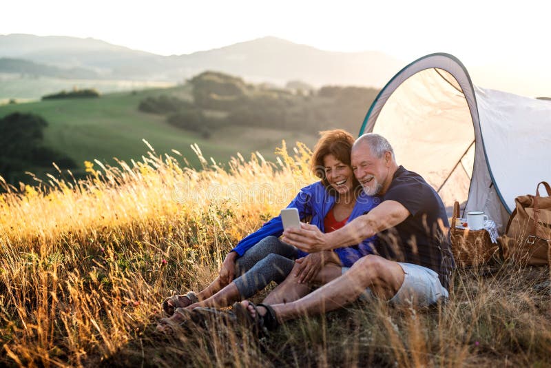 Senior tourist couple with smartphone sitting in nature at sunset, taking selfie. stock image Senior tourist couple with smartphone sitting in nature at sunset, taking selfie. stock image