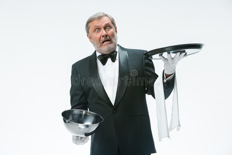 The waiter with tray and metal cloche lid cover. The senior waiter holding white towel and standing isolated on white studio background with tray and metal royalty free stock photography The waiter with tray and metal cloche lid cover. The senior waiter holding white towel and standing isolated on white studio background with tray and metal royalty free stock photography