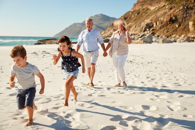 Senior white couple and their grandchildren walking on a sunny beach, close up