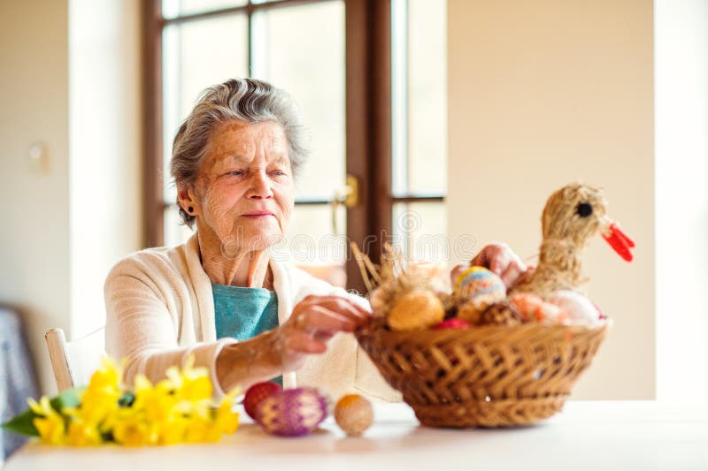 Senior woman arranging basket with Easter eggs and daffodils