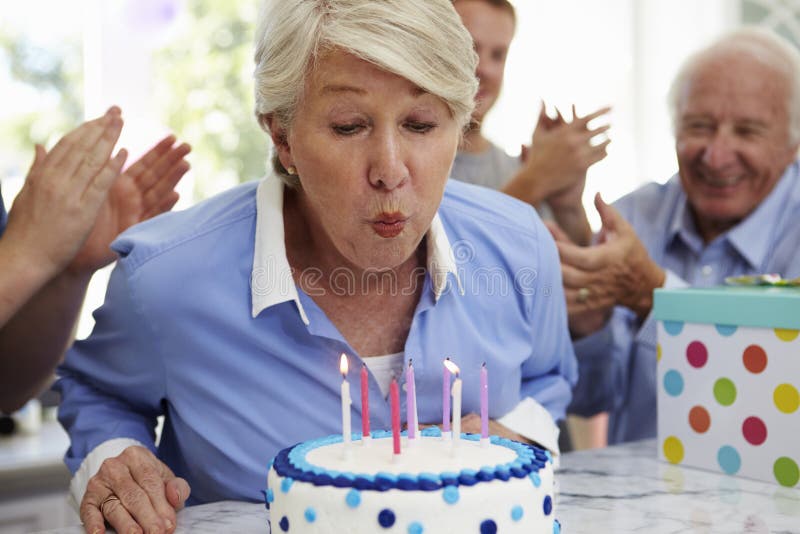 Senior Woman Blows Out Birthday Cake Candles At Family Party royalty free stock photo Senior Woman Blows Out Birthday Cake Candles At Family Party royalty free stock photo