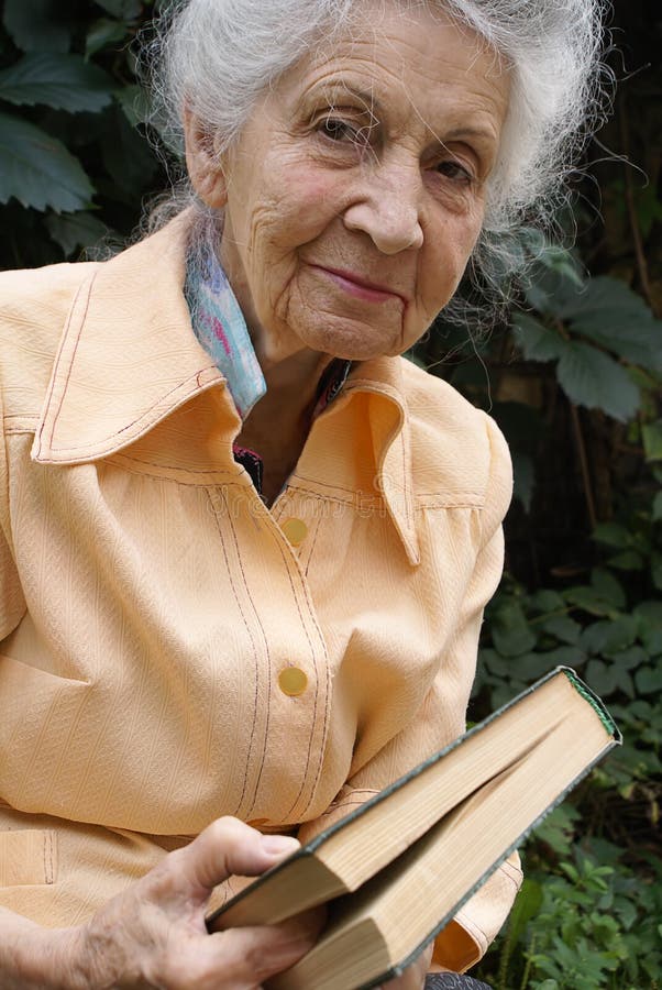 Smiling senior woman with book on green leaves background