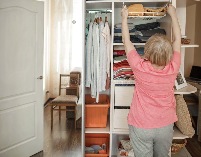 Senior woman choosing outfit from wardrobe. Cleaning, organizing and order in the closet