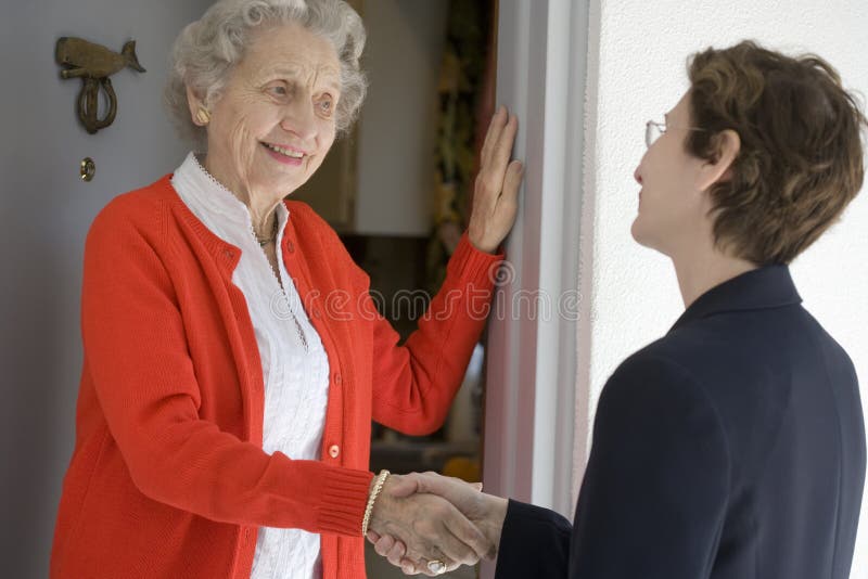 Atraktivní senior žena třesoucíma se rukama se návštěvník na její přední dveře.