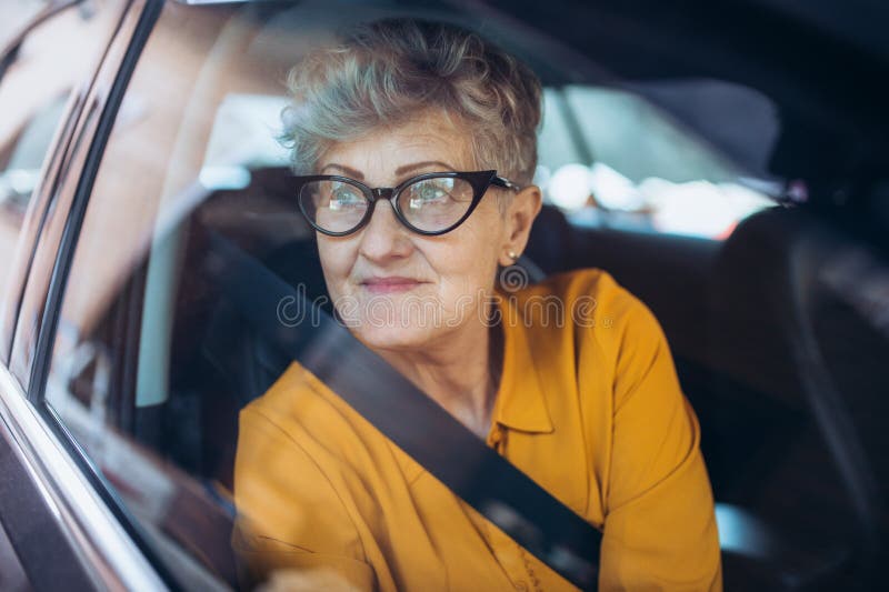 Senior woman with glasses sitting in a car. Shot through glass.