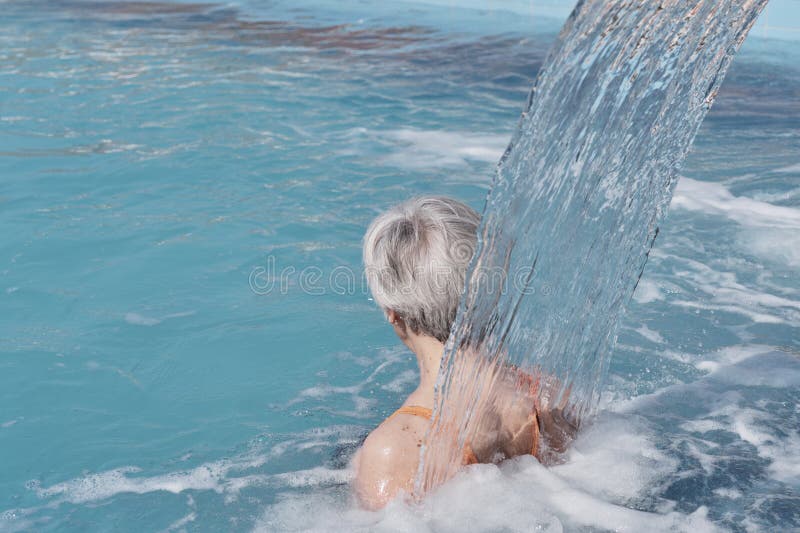 Senior woman with gray hair under flow of water falling from above. Rear view.