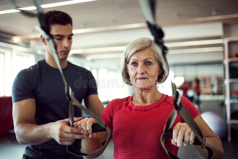 A senior woman in gym with a young trainer doing exercise with TRX. stock images A senior woman in gym with a young trainer doing exercise with TRX. stock images