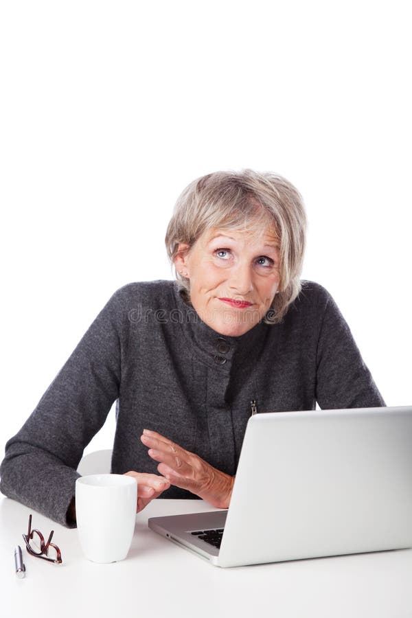 Senior woman having trouble with her computer shrugging her shoulders and looking to heaven for inspiration as she sits in front of her laptop