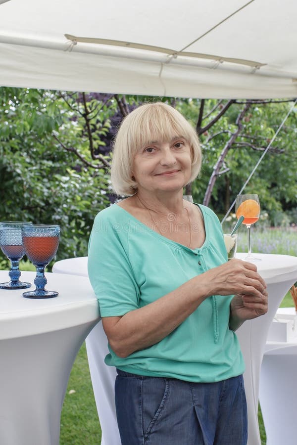 Senior woman holding a glass of colorful drink during backyard retirement party at summer