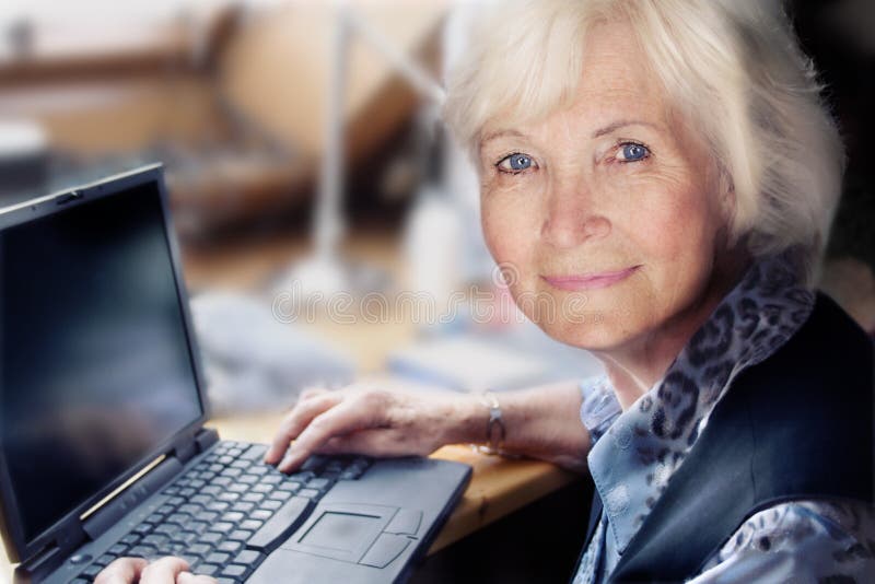 Senior signora seduta sul suo workingplace, pronto per iniziare il suo computer portatile.