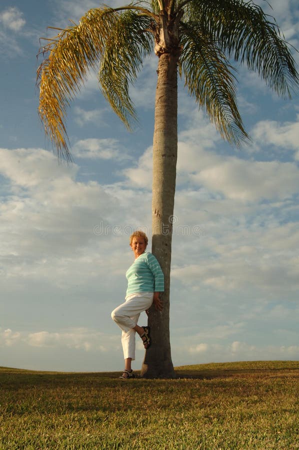Senior woman leaning against palm tree