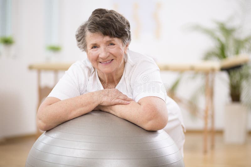 Senior woman leaning on grey gymnastic ball at physiotherapy center royalty free stock image Senior woman leaning on grey gymnastic ball at physiotherapy center royalty free stock image