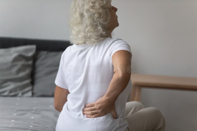 Senior woman massages her back to relieve lower back pain