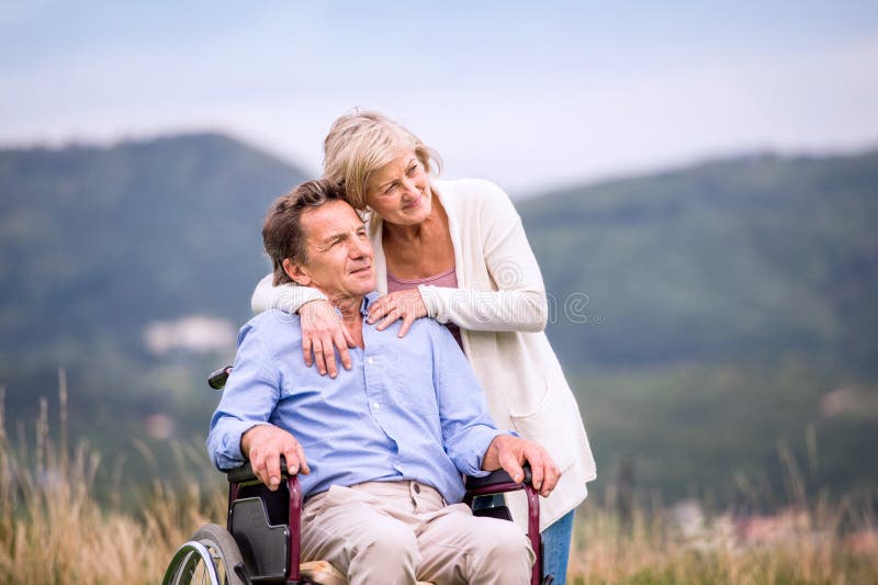 Senior woman pushing man in wheelchair, green autumn nature