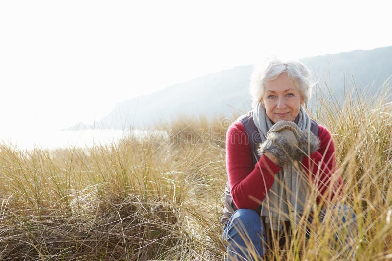 Senior Woman Walking Through Sand Dunes On Winter Beach