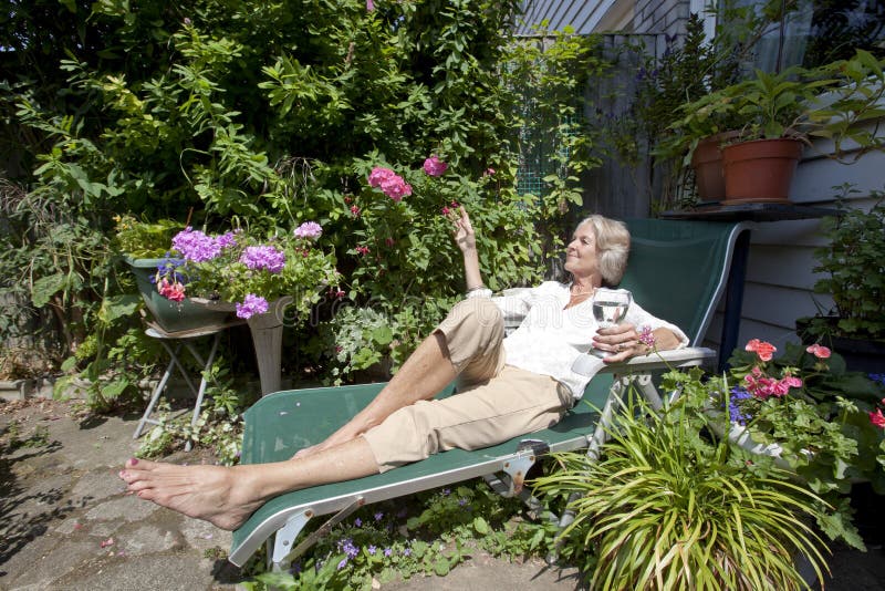 Senior woman with wineglass relaxing on lounge chair in garden