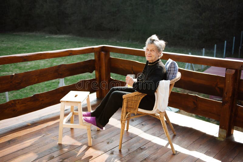 Senior woman on wooden terrace, resting with feet up.