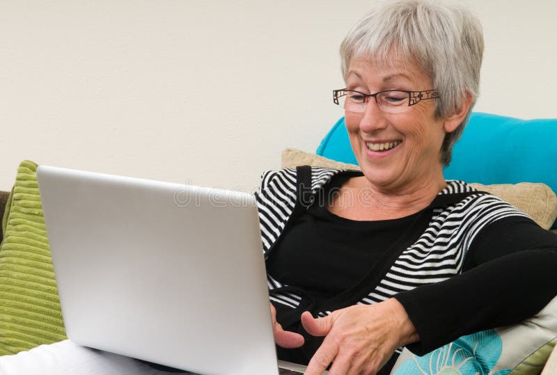 Senior woman working on a laptop, sitting relaxed on the couch.