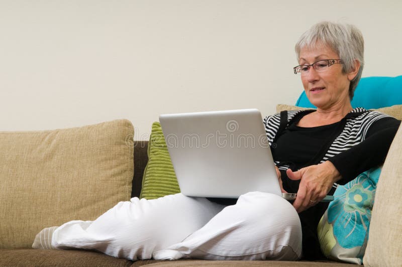 Senior woman working on a laptop, sitting relaxed on the couch.
