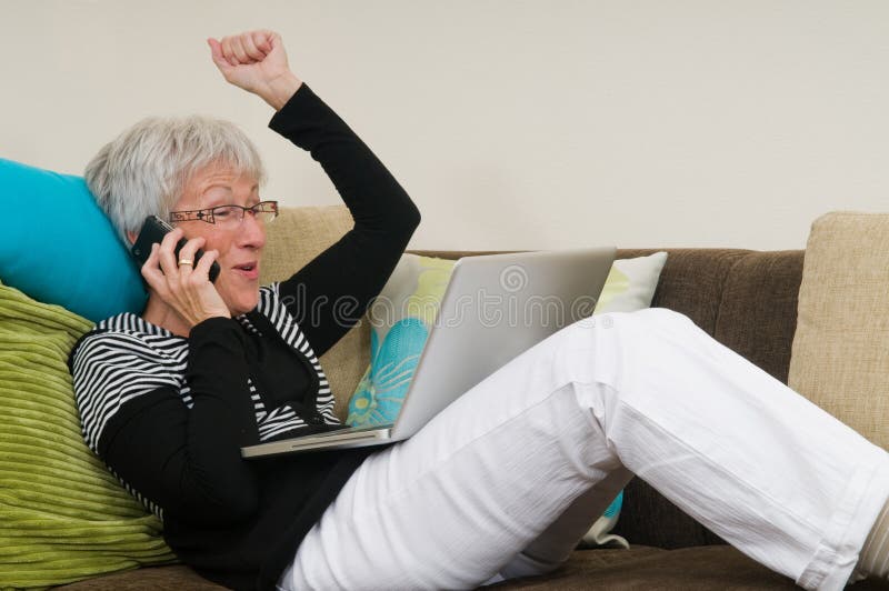 Senior woman working on a laptop, lying relaxed on the couch.