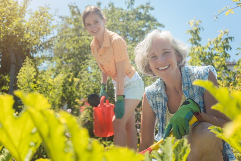 Senior woman working in the vegetables while daughter is watering garden