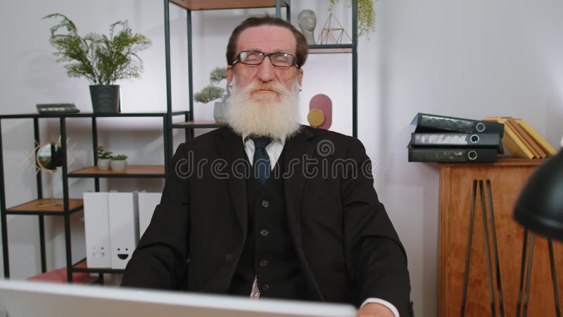Senior älterer Geschäftsmann arbeitet auf Laptop im Büro mit Ohrhörern und hört Lieblings-Diskothek