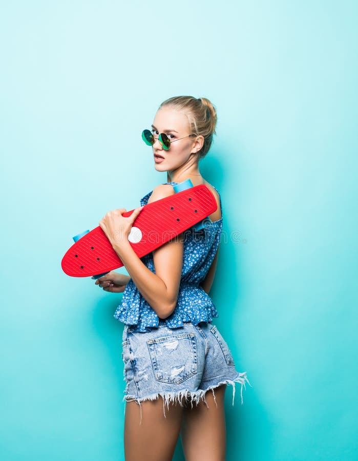 Sensación libre y feliz Mujer joven atractiva en gafas de sol que sonríe y que lleva el monopatín mientras que se opone a backgro fotografía de archivo libre de regalías Sensación libre y feliz Mujer joven atractiva en gafas de sol que sonríe y que lleva el monopatín mientras que se opone a backgro fotografía de archivo libre de regalías