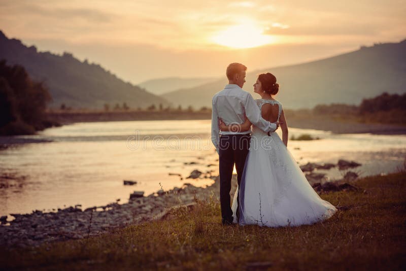 Sensitive wedding back shot. Peaceful beautiful newlyweds are hugging and looki at each other on the river bank during stock photography Sensitive wedding back shot. Peaceful beautiful newlyweds are hugging and looki at each other on the river bank during stock photography