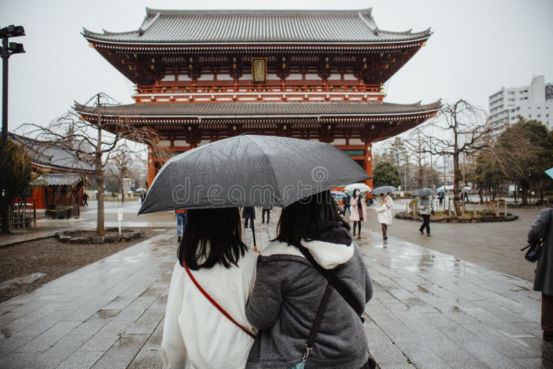 Sensoji Temple - Tokyo, Japan - February 16, 2020: 2 Asian women stay looking in front of Sensoji Temple and holding 1 black